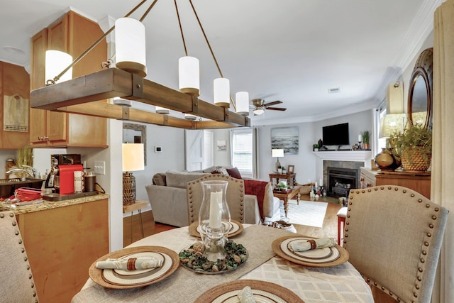 dining area with ceiling fan, a fireplace, ornamental molding, and wood-type flooring