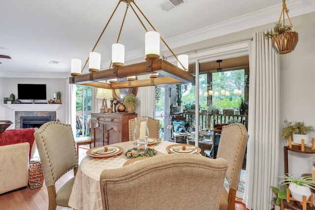 dining area featuring wood-type flooring, a tiled fireplace, plenty of natural light, and crown molding