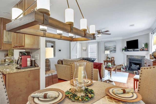 dining room with a fireplace, ceiling fan, hardwood / wood-style flooring, ornamental molding, and sink