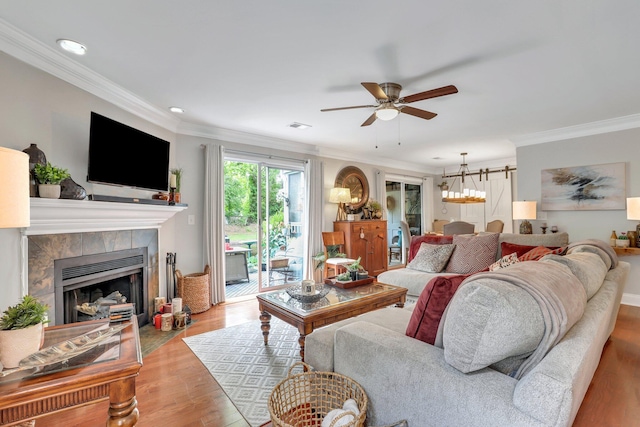 living room featuring light wood-type flooring, a tile fireplace, ceiling fan with notable chandelier, and crown molding