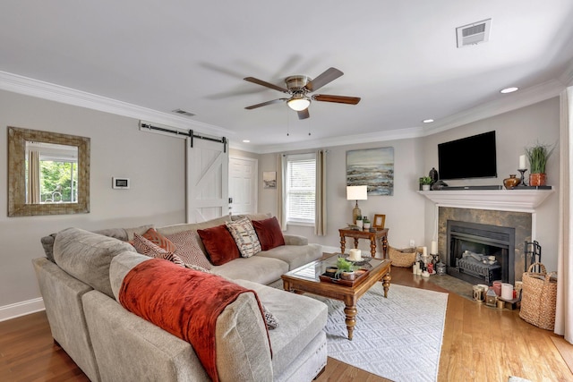 living room with ceiling fan, wood-type flooring, a tile fireplace, crown molding, and a barn door