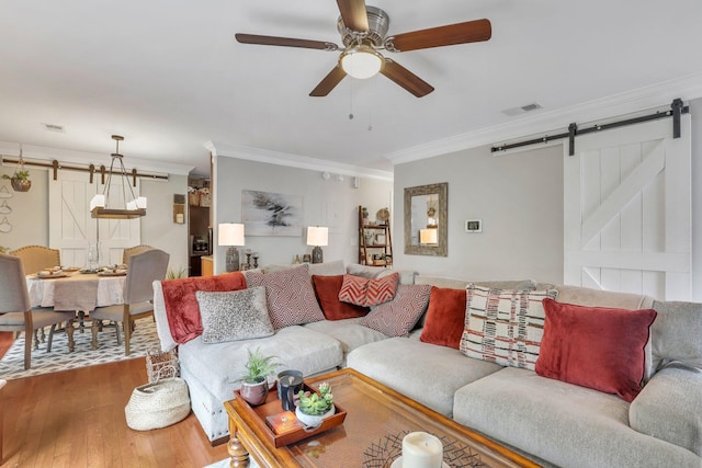 living room with wood-type flooring, ceiling fan, crown molding, and a barn door