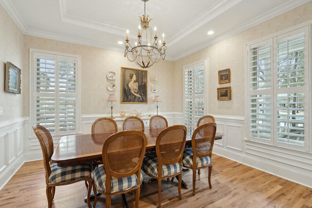 dining room featuring a chandelier, a raised ceiling, wainscoting, and light wood-style flooring