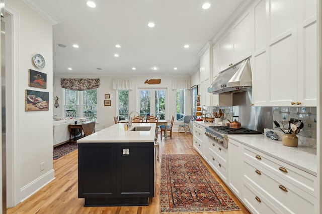 kitchen featuring under cabinet range hood, a center island with sink, white cabinets, and a sink