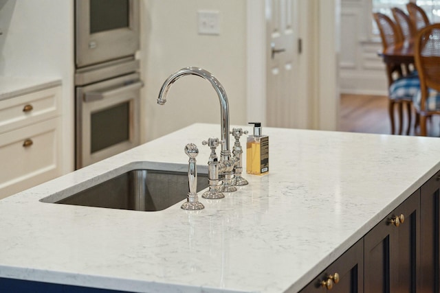 details with dark brown cabinets, stainless steel oven, a sink, and light stone countertops