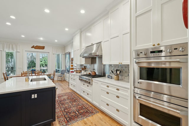 kitchen with under cabinet range hood, stainless steel appliances, a sink, white cabinetry, and an island with sink