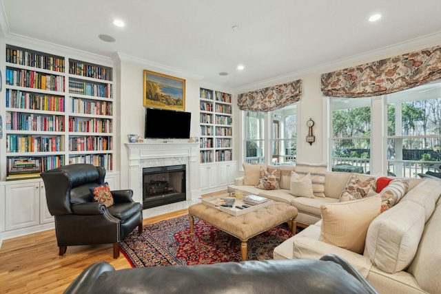 living room featuring built in features, crown molding, recessed lighting, a premium fireplace, and light wood-style floors