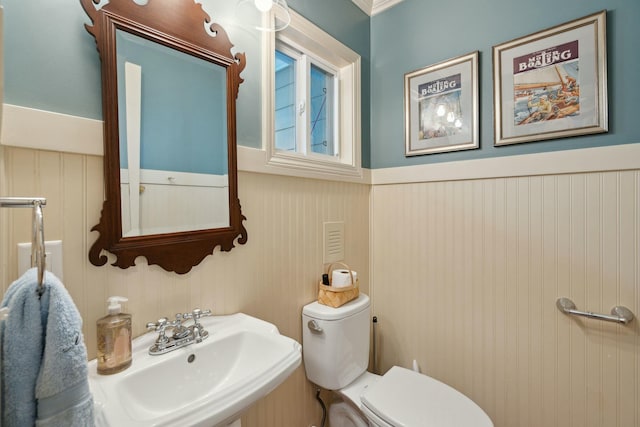 half bathroom with a wainscoted wall, a sink, and toilet