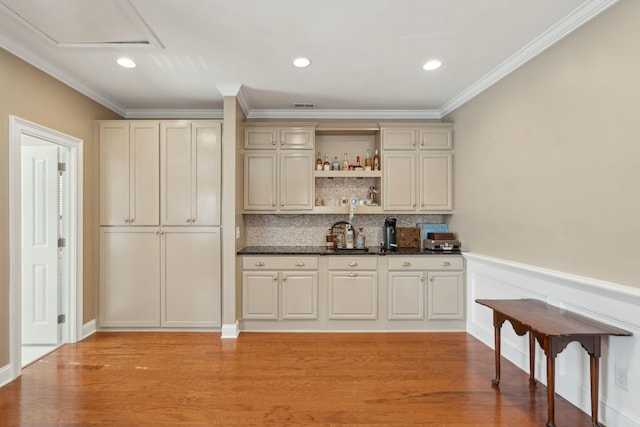 bar with light wood finished floors, indoor wet bar, and crown molding