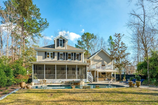 rear view of house featuring a patio, a lawn, a pool with connected hot tub, and a sunroom