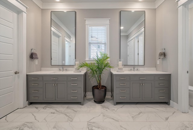 bathroom featuring marble finish floor, toilet, a sink, and two vanities