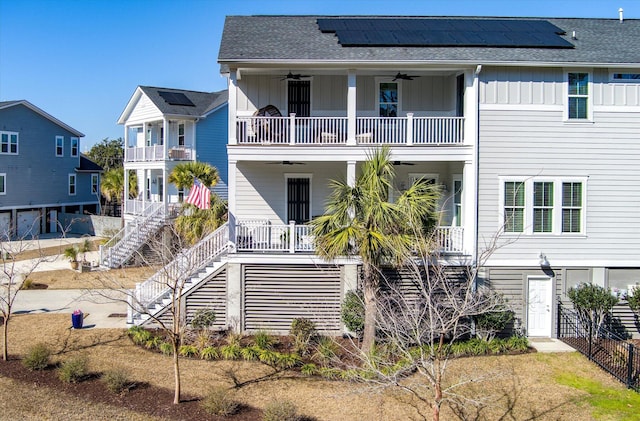 view of front of property featuring stairway, ceiling fan, board and batten siding, roof mounted solar panels, and a porch