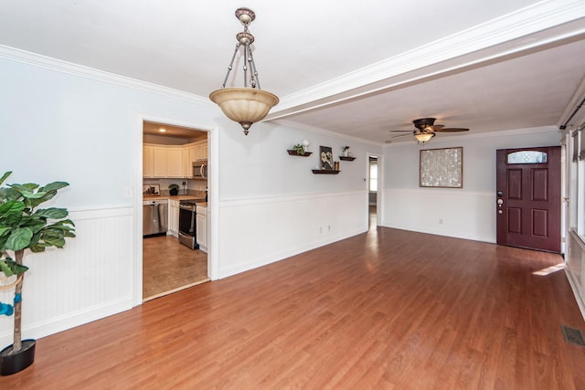 unfurnished living room with wainscoting, wood finished floors, a ceiling fan, and crown molding