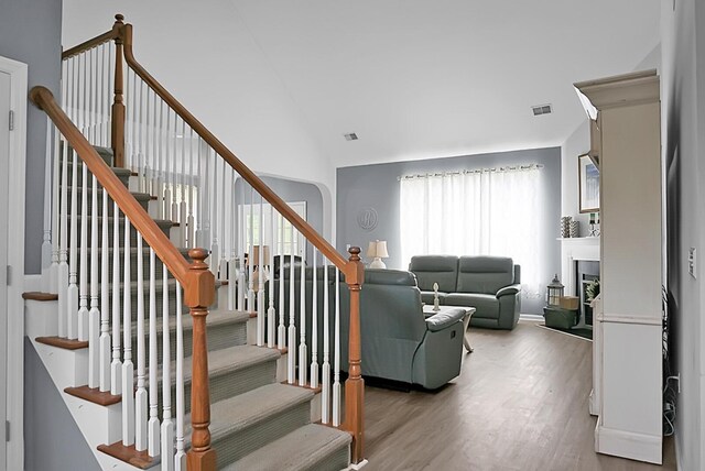 staircase featuring wood finished floors, a fireplace, and lofted ceiling