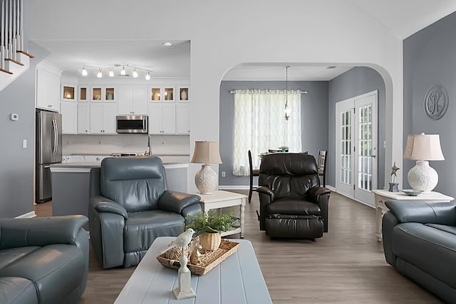 living area featuring arched walkways, wood finished floors, vaulted ceiling, and baseboards