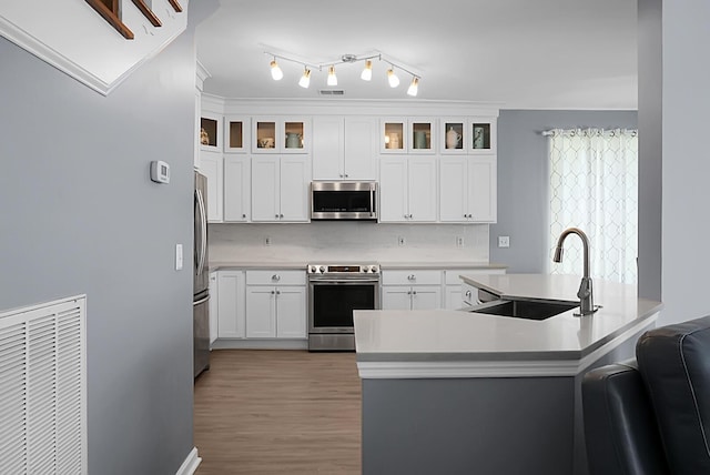 kitchen with stainless steel appliances, a sink, backsplash, light countertops, and light wood-style flooring