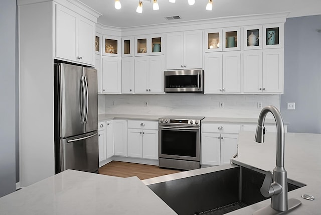 kitchen with appliances with stainless steel finishes, a sink, light countertops, and tasteful backsplash