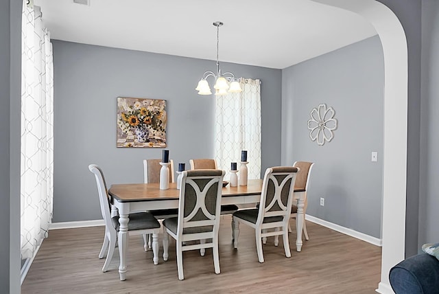 dining space with a chandelier, wood finished floors, baseboards, and arched walkways