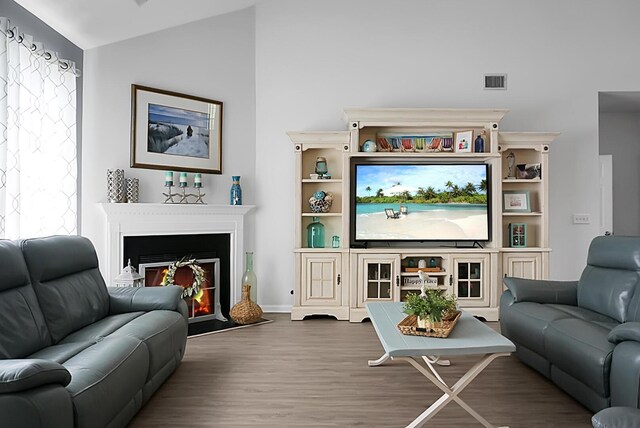living room featuring lofted ceiling, wood finished floors, a warm lit fireplace, and baseboards