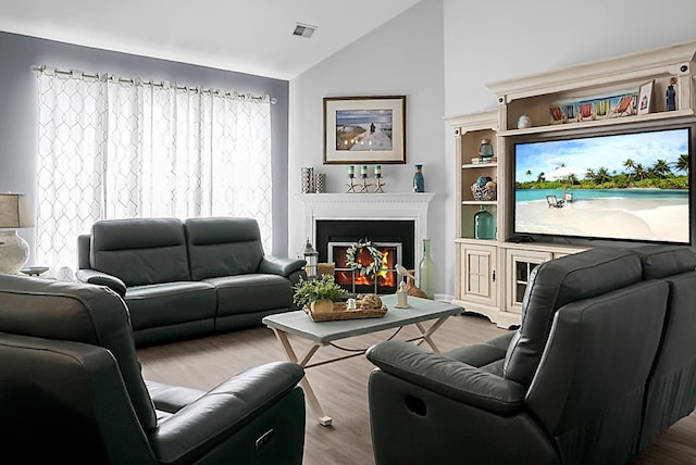 living area with lofted ceiling, wood finished floors, a warm lit fireplace, and healthy amount of natural light