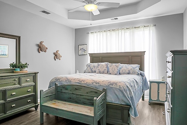 bedroom featuring dark wood-style flooring, a raised ceiling, ceiling fan, and baseboards