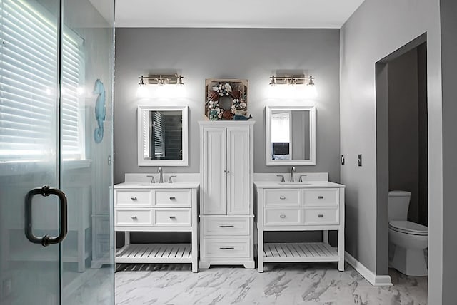 full bath with marble look tile flooring, two vanities, baseboards, a shower stall, and toilet
