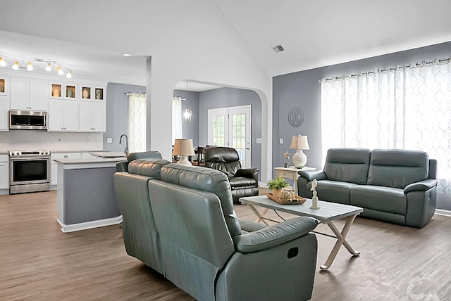 living area featuring arched walkways, wood finished floors, high vaulted ceiling, and baseboards