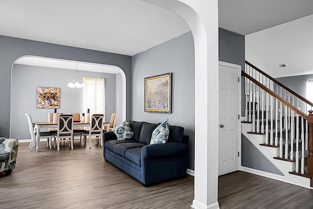 living room featuring arched walkways, wood finished floors, a chandelier, stairway, and baseboards