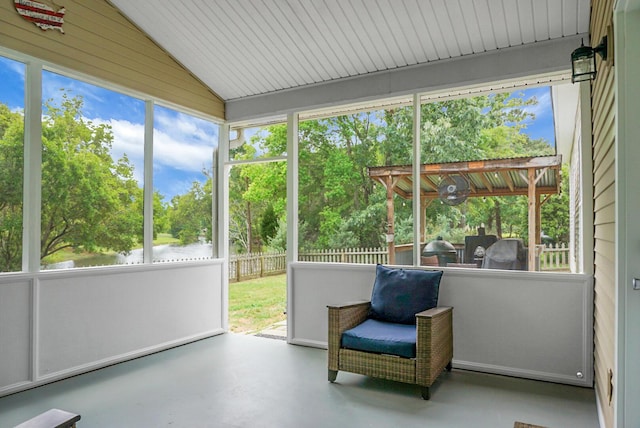 sunroom with lofted ceiling, view of wooded area, and a water view