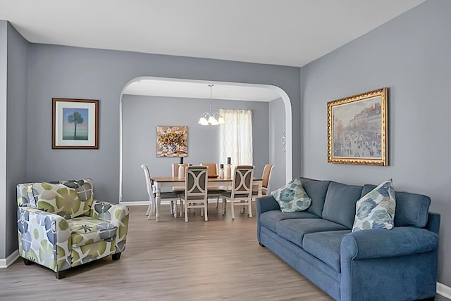 living room featuring arched walkways, a chandelier, wood finished floors, and baseboards