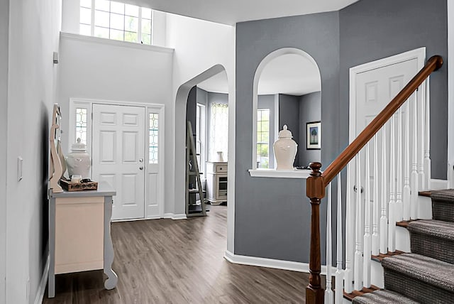 foyer featuring baseboards, wood finished floors, arched walkways, and stairway