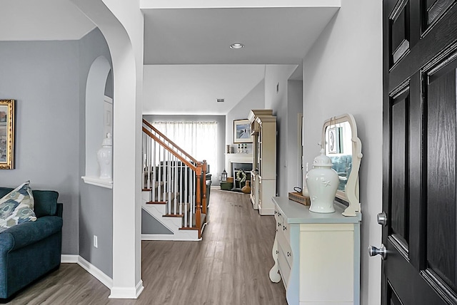 entryway featuring light wood-style flooring, stairs, baseboards, and arched walkways
