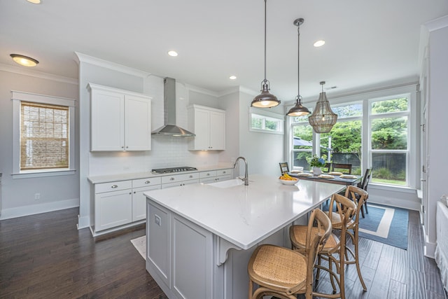 kitchen featuring wall chimney range hood, gas cooktop, ornamental molding, a sink, and tasteful backsplash