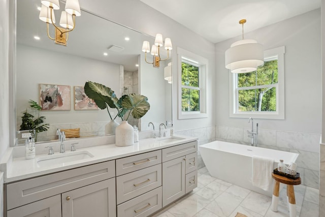 full bathroom with an inviting chandelier, a freestanding tub, marble finish floor, and a sink
