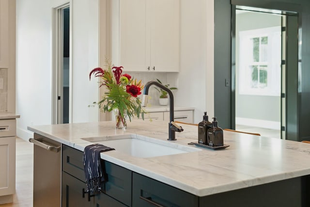 kitchen featuring tasteful backsplash, stainless steel dishwasher, light stone counters, sink, and white cabinetry