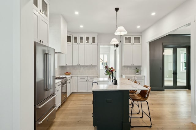 kitchen with high end appliances, a kitchen island with sink, sink, decorative light fixtures, and white cabinetry