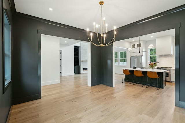 kitchen featuring high end appliances, a kitchen island with sink, decorative light fixtures, white cabinets, and a chandelier