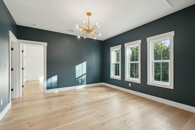 empty room featuring a notable chandelier and light hardwood / wood-style flooring