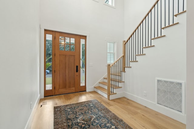 entrance foyer with a towering ceiling, a healthy amount of sunlight, and light hardwood / wood-style floors