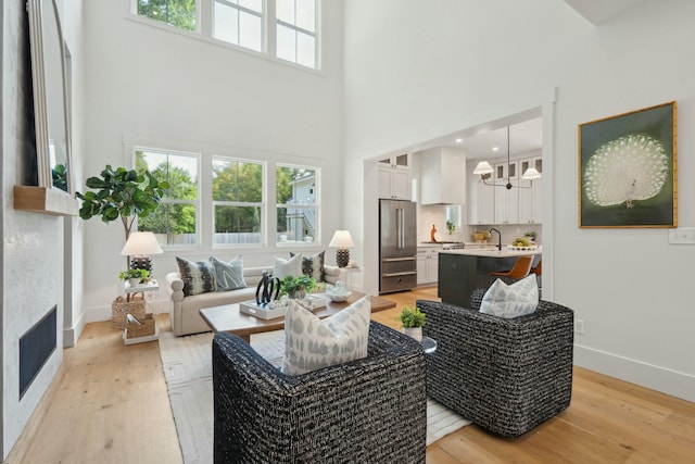 living area with a fireplace, light wood-style flooring, a towering ceiling, a notable chandelier, and baseboards