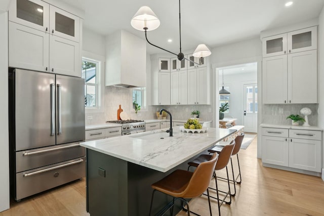 kitchen featuring light wood-style flooring, premium range hood, high end appliances, white cabinets, and light stone countertops