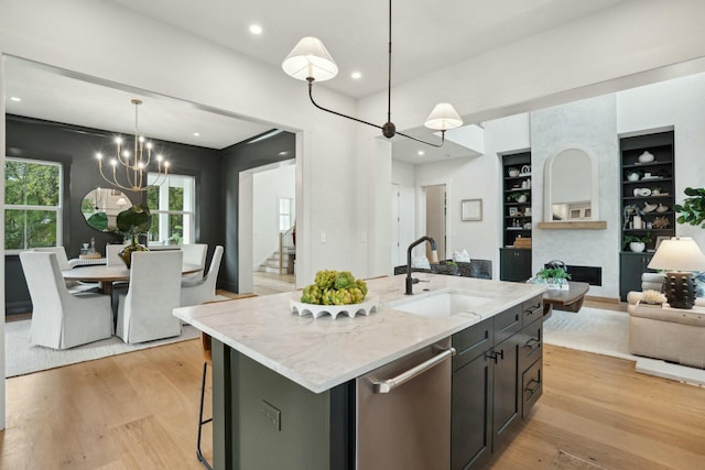 kitchen featuring light wood-style floors, stainless steel dishwasher, a sink, open floor plan, and a notable chandelier