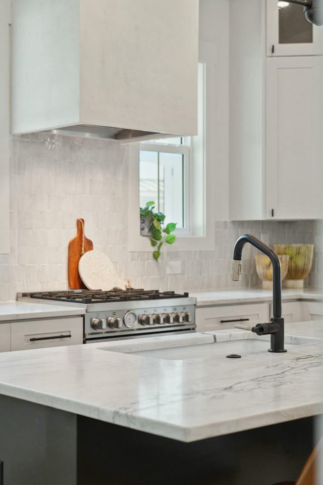 kitchen with stainless steel gas stove, light stone counters, custom range hood, and white cabinetry
