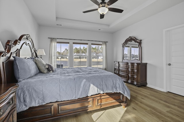 bedroom with ceiling fan, a raised ceiling, and hardwood / wood-style floors