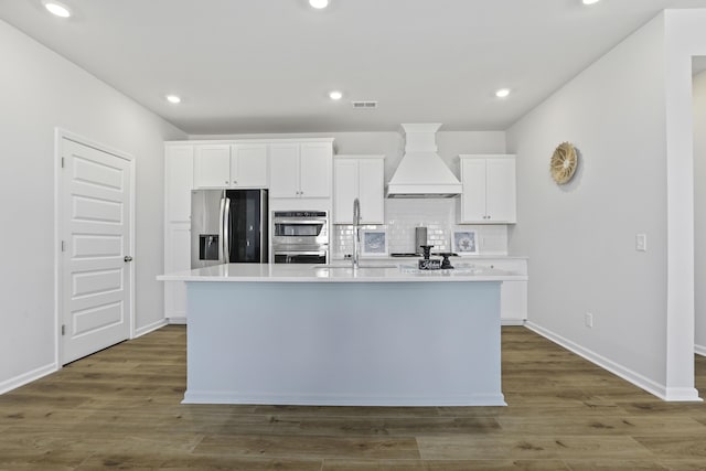 kitchen featuring sink, white cabinetry, stainless steel appliances, custom range hood, and an island with sink