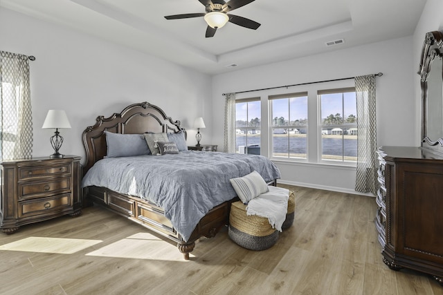 bedroom with ceiling fan, a tray ceiling, and light wood-type flooring