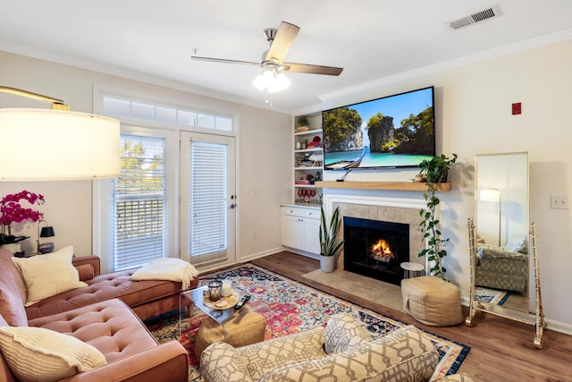 living room with crown molding, hardwood / wood-style flooring, and a tiled fireplace