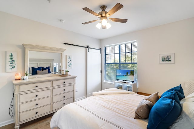 bedroom featuring ceiling fan, light hardwood / wood-style flooring, and a barn door