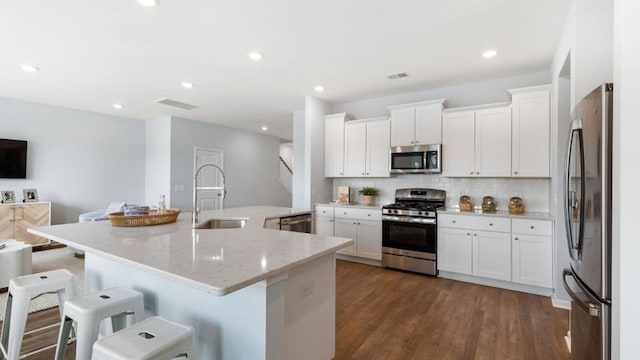 kitchen featuring stainless steel appliances, a sink, white cabinetry, decorative backsplash, and dark wood-style floors