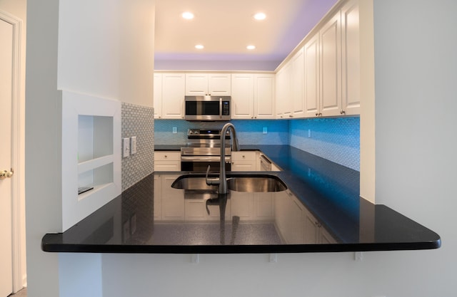 kitchen featuring sink, appliances with stainless steel finishes, tasteful backsplash, white cabinets, and kitchen peninsula